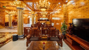 A spacious lobby with ornate wooden columns, a large chandelier, and a television on the right. - Nam Hong Hotel (Binh Nguyen)