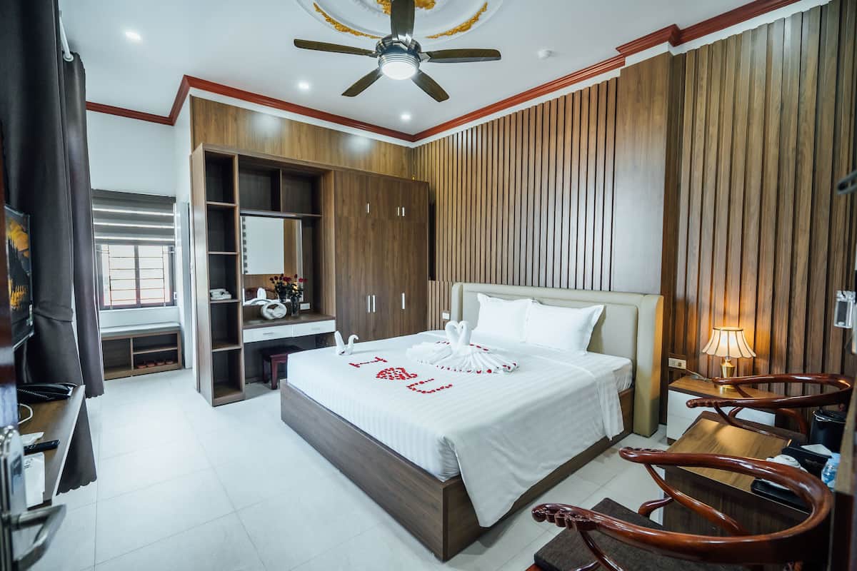 Une chambre d’hôtel avec un grand lit, des lambris en bois aux murs, un ventilateur de plafond et un bureau avec une lampe.