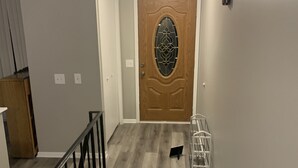 Un pasillo con puerta de madera, barandilla metálica y pared blanca.