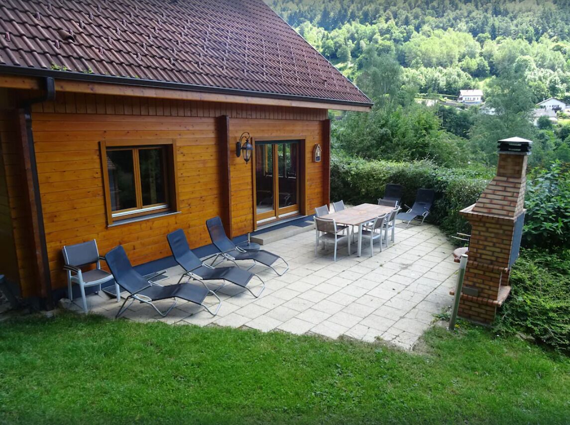 Une maison en bois avec un patio carrelé, un espace salon extérieur et une cheminée.