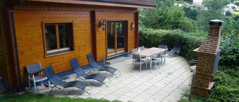 Une maison en bois avec un patio carrelé, un espace salon extérieur et une cheminée.