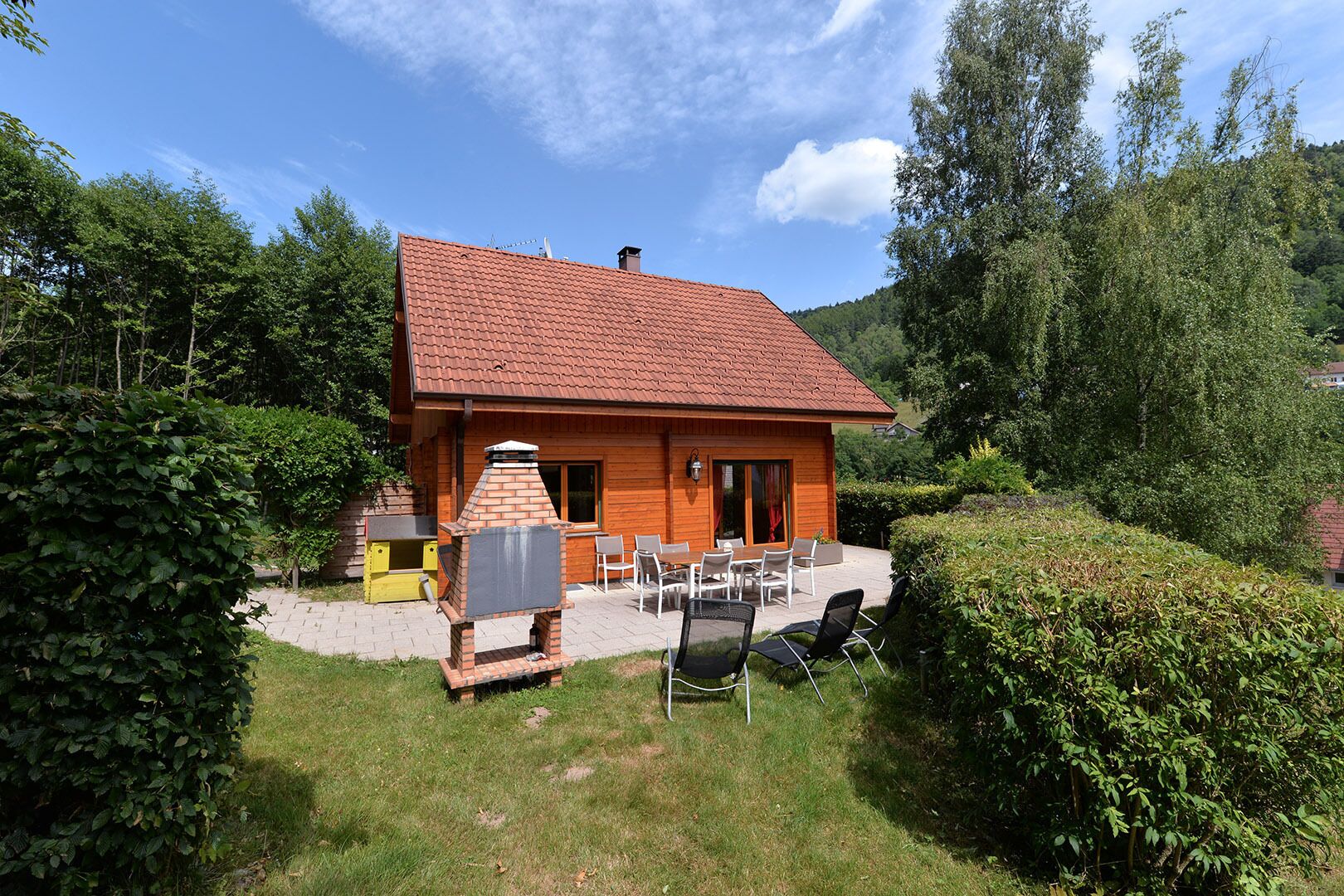 A wooden house with a tiled roof, a brick oven, and a patio with outdoor seating.