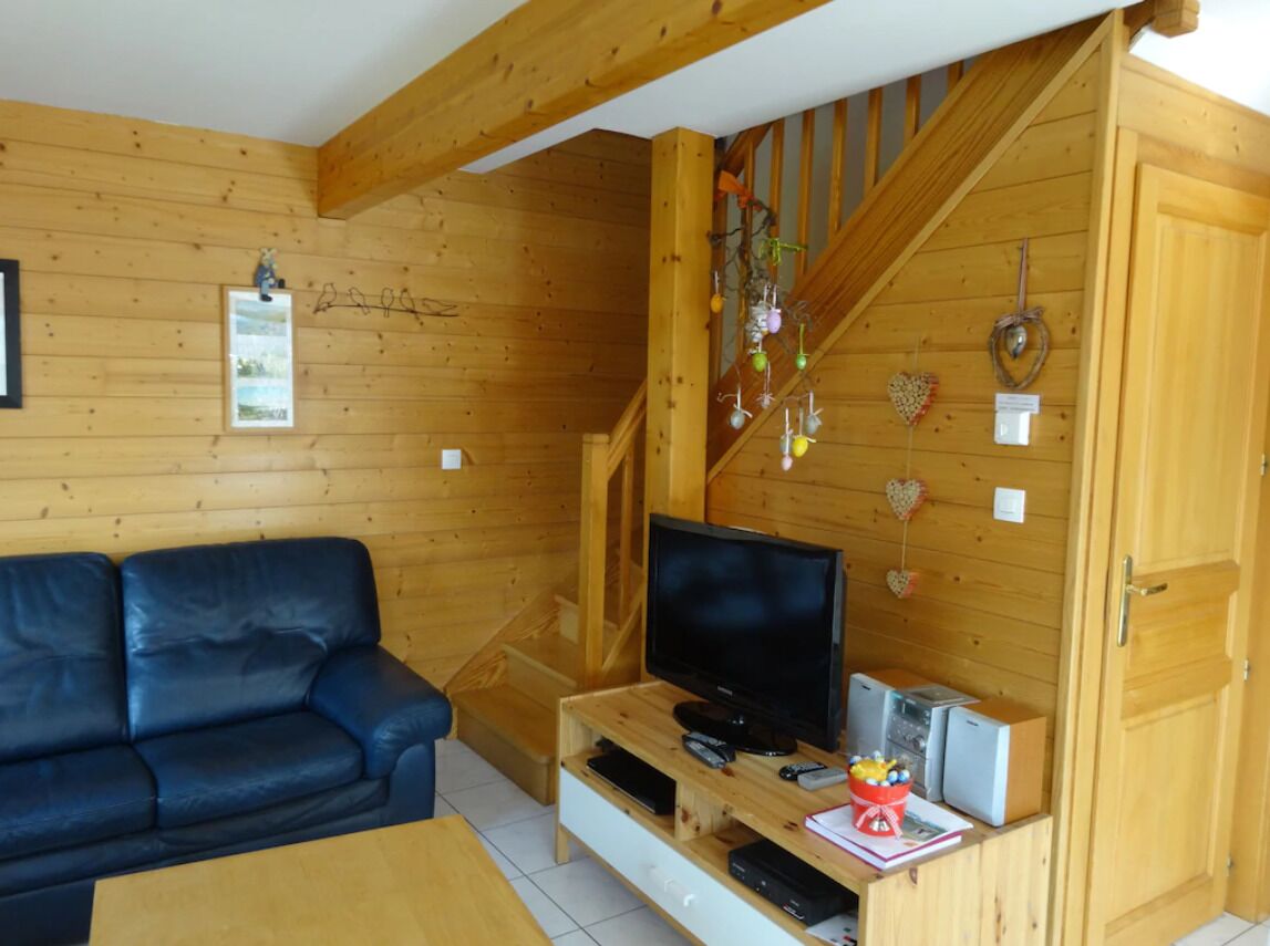 Un intérieur en bois avec un canapé, un téléviseur posé sur un meuble en bois et un escalier.
