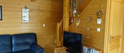 Un intérieur en bois avec un canapé, un téléviseur posé sur un meuble en bois et un escalier.
