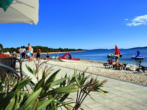 Een strandgebied met een verhard pad, ligbedden en parasols.