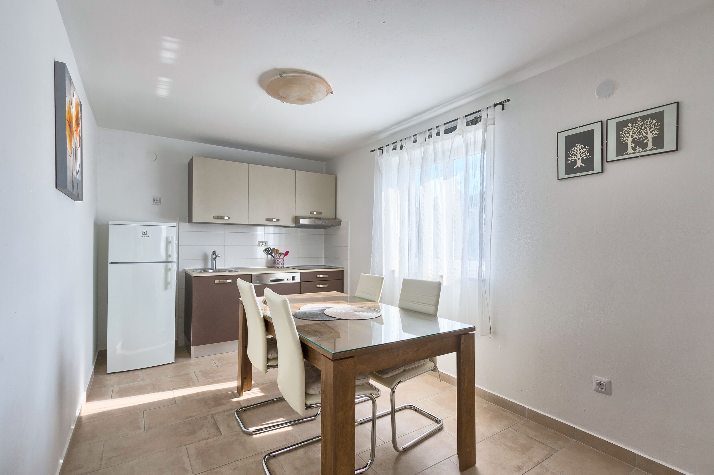 A modern kitchen with white cabinets, a built-in oven, and a dining area with a glass table and chairs.