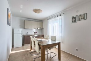 Una cocina moderna con armarios blancos, horno empotrado y comedor con mesa y sillas de vidrio.