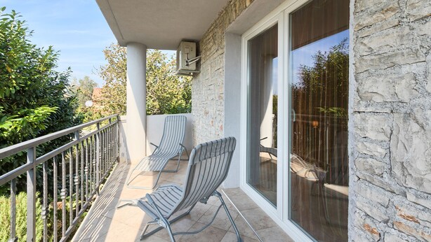 Een balkon met twee gestreepte stoelen, een stenen muur en een glazen deur naar een terras.