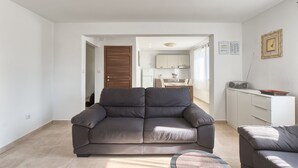 Een moderne woonkamer met een grijze bank, een klein rond tafeltje en een keuken op de achtergrond.