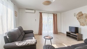Een moderne woonkamer met een grijze bank, een klein rond tafeltje en een tv op een houten dressoir.