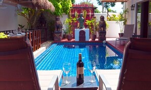 Relax by the serene pool surrounded by lush greenery and a thatched roof structure.
