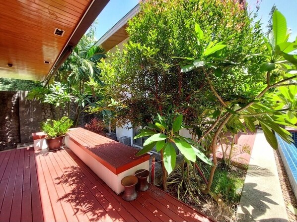 Relax in a serene outdoor space with a deck leading to a cozy seating area surrounded by lush greenery and a pool.