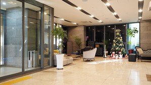 Un hall d’entrée moderne avec un mur de verre, un sapin de Noël et des espaces aménagés pour s’asseoir.