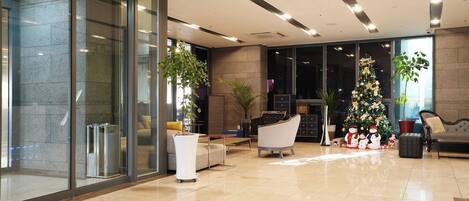 Um lobby moderno com parede de vidro, árvore de Natal e áreas de estar.