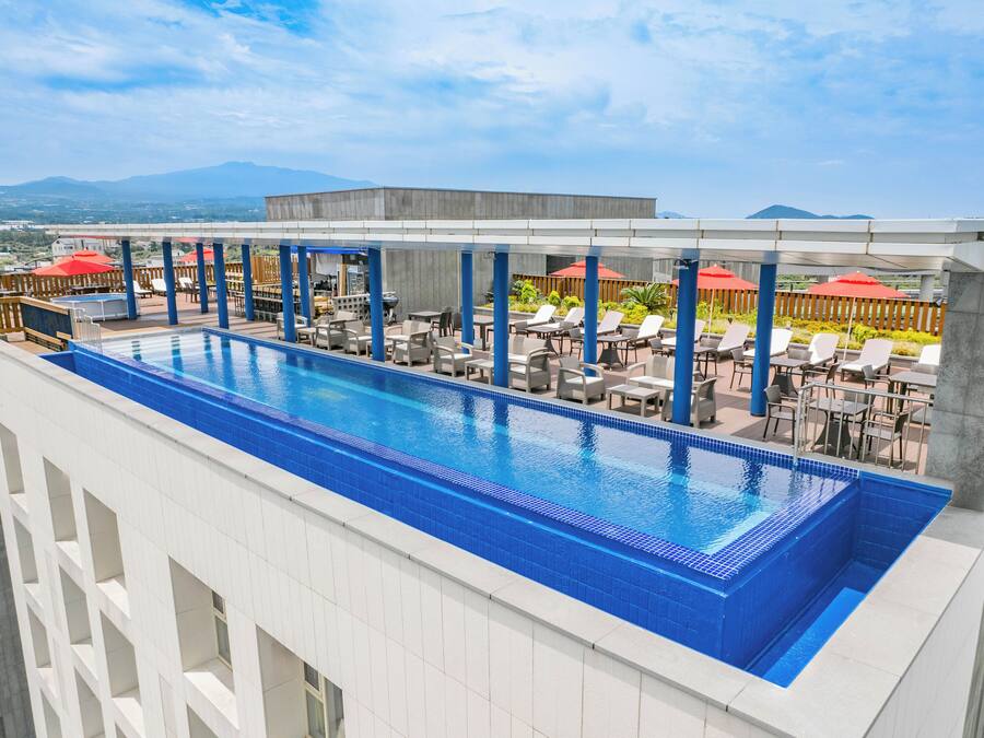En pool på taket med blå kakelplattor, omgiven av solstolar och parasoller, med utsikt över berg i bakgrunden.