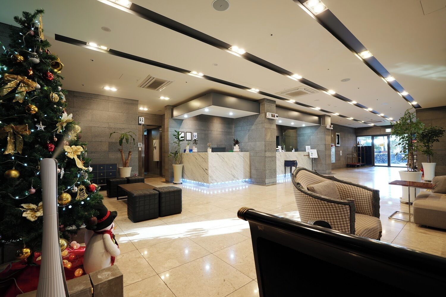 A modern hotel lobby with a reception desk, seating area, and a Christmas tree.