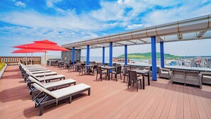 Une terrasse sur le toit, dotée de chaises longues, de parasols rouges et de tables, offrant une vue sur le paysage urbain.