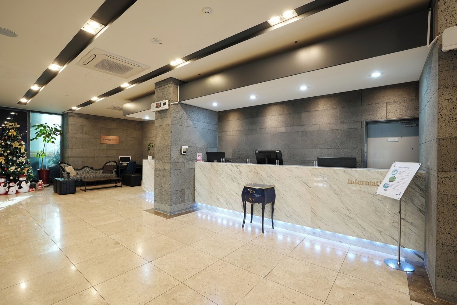 A hotel reception area with a marble counter, a seating area with a sofa and chairs, and a Christmas tree.