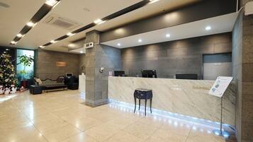A hotel reception area with a marble counter, a seating area with a sofa and chairs, and a Christmas tree.