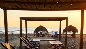 Un espace de détente aménag é sur la plage, avec des chaises longues et des parasols en chaume, offrant une vue sur l’océan.