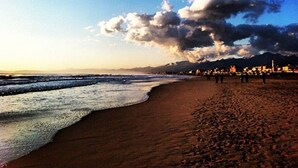 Une plage avec un large rivage sablonneux, des vagues et, au loin, une vue sur la ville avec ses bâtiments et ses montagnes.