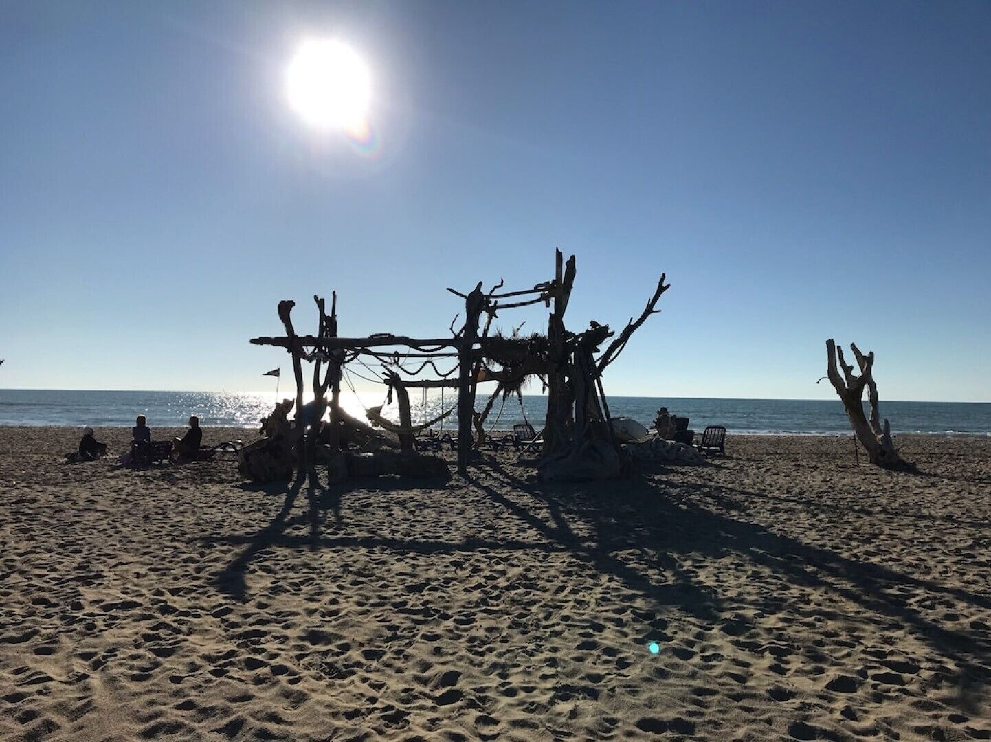 Uma praia com uma estrutura de madeira e pessoas sentadas na areia.