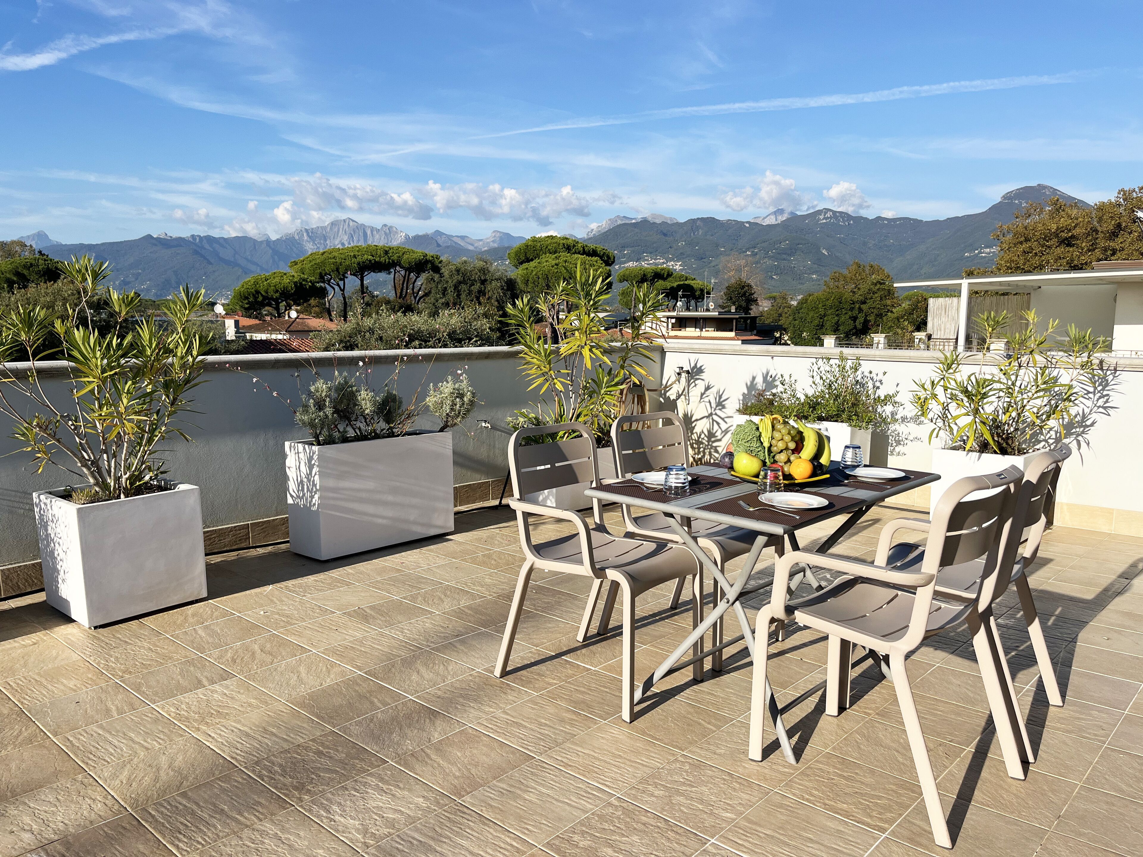 An outdoor patio with a table and chairs, surrounded by potted plants, overlooking a scenic mountain view.