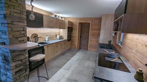 A modern kitchen with wooden cabinets, a stone accent wall, and a black countertop. - Mountain chalet rental ★★★★ "La Boutame" (Alpe d'Huez Domain 3300m) (Villard-Reculas)