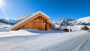 Un chalet en bois, doté d’un toit à pente, entouré de montagnes enneigées et surplombant un ciel dégagé.