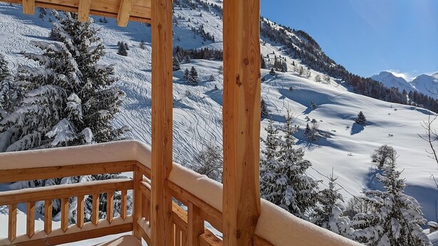 Un balcon en bois offrant une vue sur un paysage montagneux enneigé.