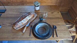Une table de salle à manger en bois, avec une miche de pain, un couteau, une fourchette, un verre et une assiette.
