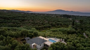 A modern house with a swimming pool, surrounded by dense greenery and overlooking a coastal landscape.