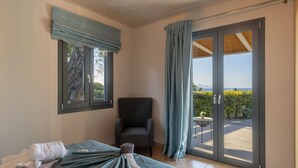 A bedroom with a bed, a chair, a window with a view, and a sliding glass door to a balcony.