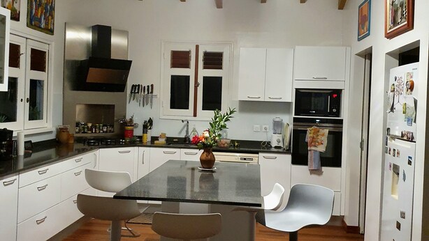 A modern kitchen with white cabinets, a central island with bar stools, a built-in oven, and a refrigerator with magnets.