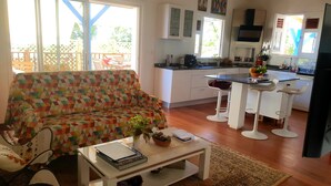 A modern kitchen with white cabinets, a black countertop, and a built-in oven. There is a colorful patterned sofa and a small dining table with two chairs.