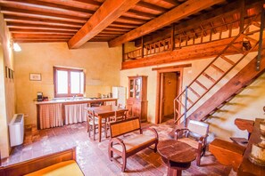 A rustic kitchen with wooden beams, a dining area with a wooden table and chairs, and a staircase leading to an upper level.