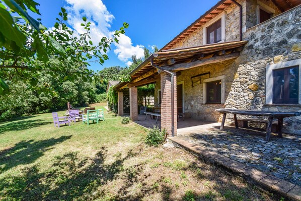 A stone house with a covered patio, outdoor seating, and a grassy yard.