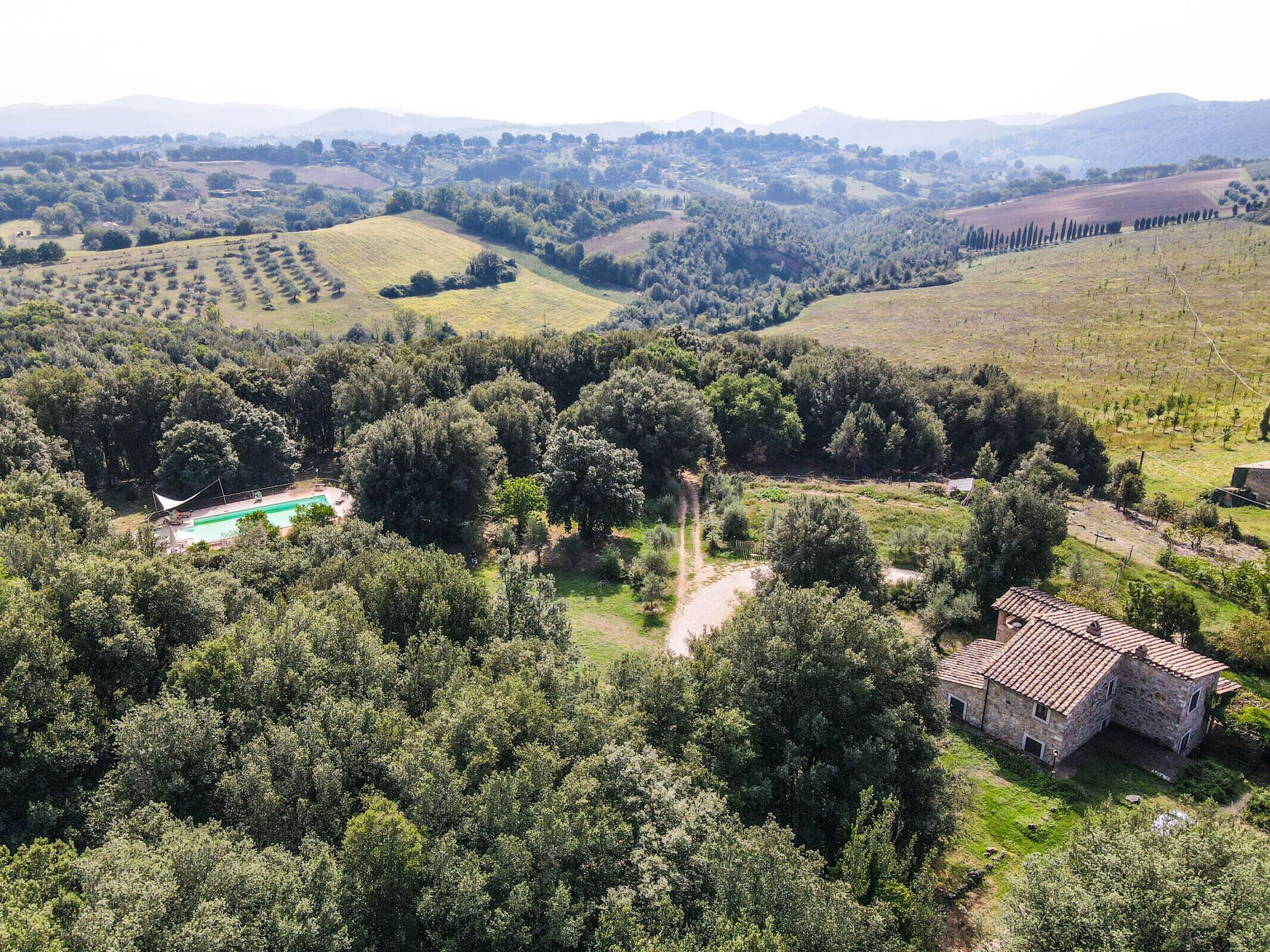 An aerial view of a rural landscape with a stone building, a swimming pool, and a vineyard.