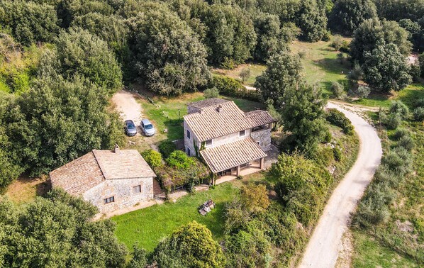 Vista aerea di una proprietà rurale con due edifici in pietra, un vialetto lastricato e vegetazione circostante.