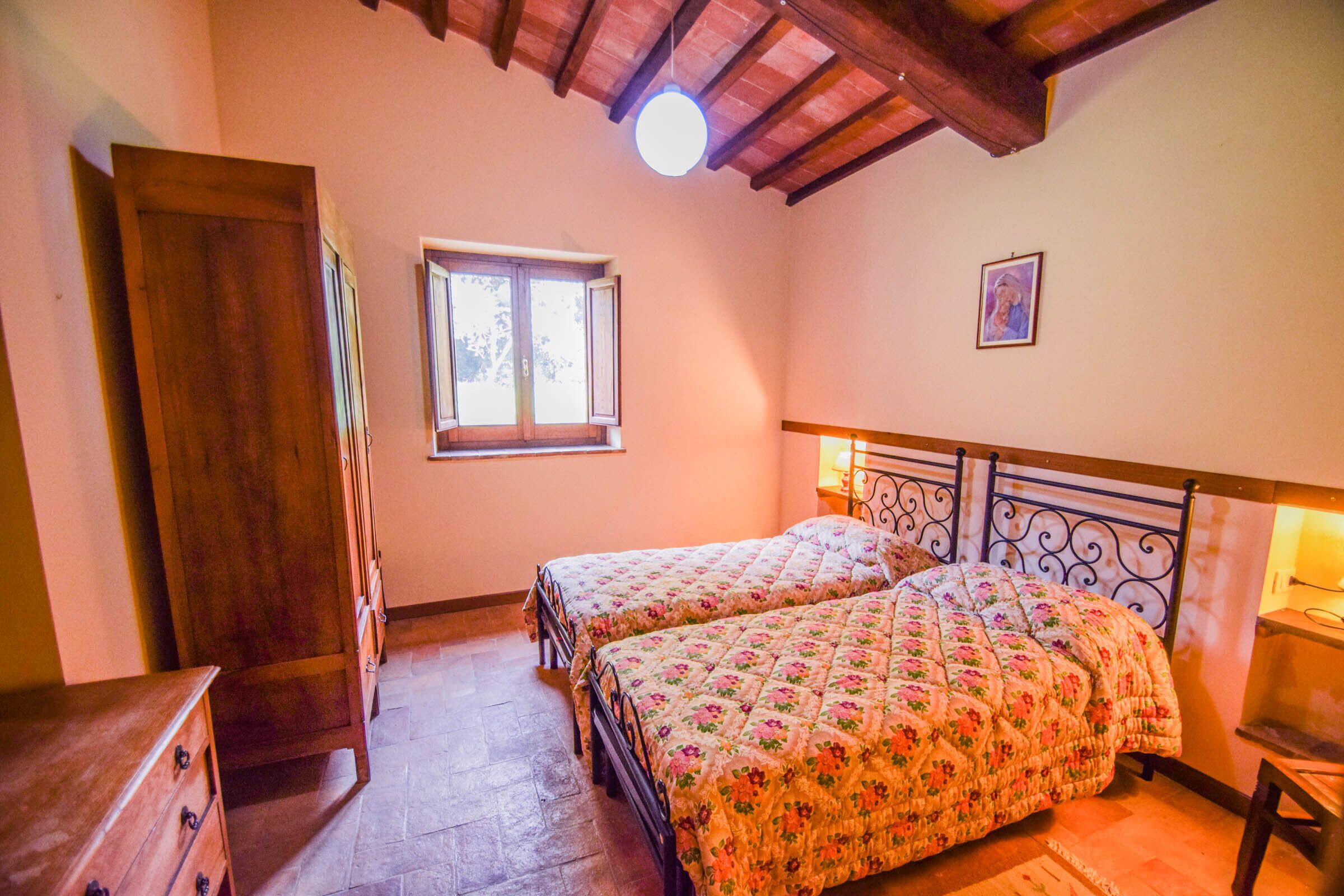 A bedroom with two beds, wooden furniture, a window, and a ceiling light.