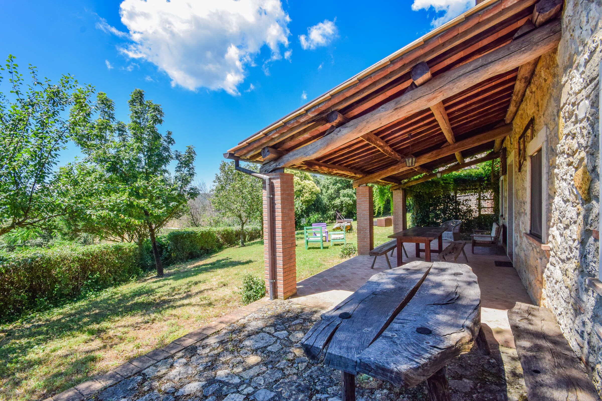 Um espaço ao ar livre coberto, com parede de pedra, bancos de madeira e mesa de piquenique.