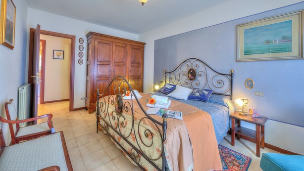 A bedroom with a bed, a chair, a nightstand, and a door leading to another room. - Casa Elisabetta 100m From Stresa Downto (Stresa)