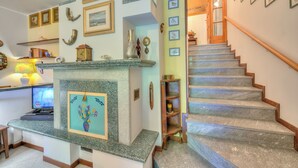 A living room with a fireplace, a staircase, and a wall decorated with framed pictures. - Casa Elisabetta 100m From Stresa Downto (Stresa)