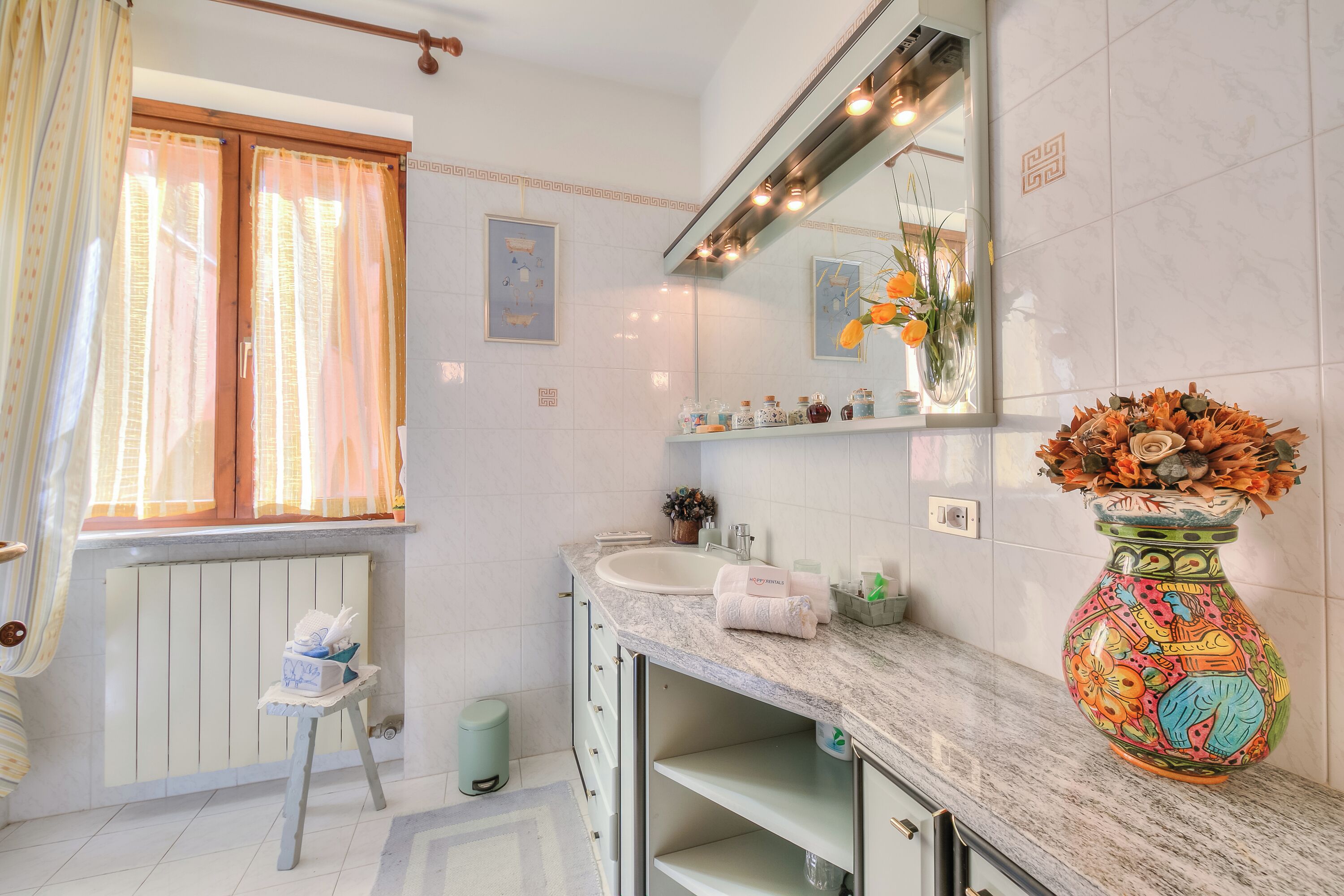 A bathroom with a marble countertop, a sink, a mirror, a vase with flowers, and a radiator.