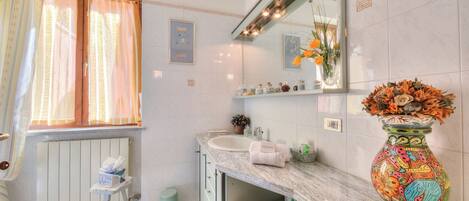 A bathroom with a marble countertop, a sink, a mirror, a vase with flowers, and a radiator.