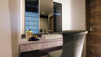 A modern bathroom with a large mirror, a white sink, and a grey chair.