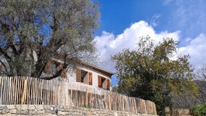 Un edificio tradicional con pared de piedra y cerca de madera, rodeado de árboles.