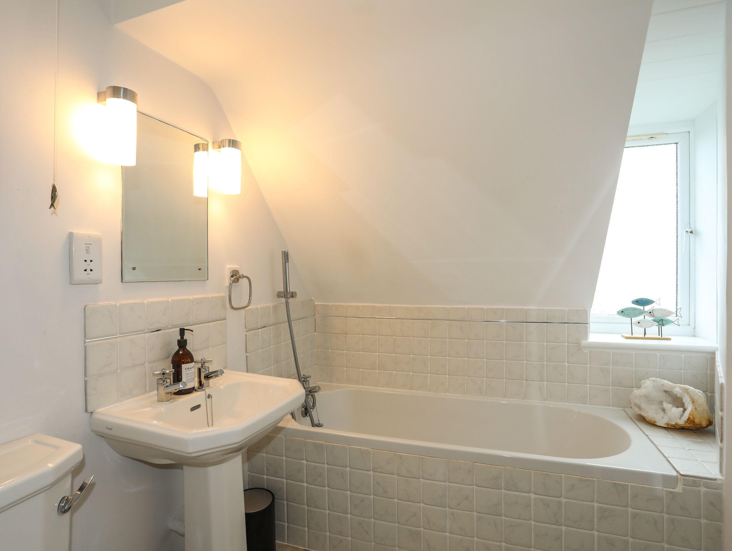 A modern bathroom with a white sink, a bathtub, and a window with a view of the sky.