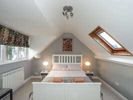A bedroom with a sloped ceiling, a skylight, a bed with two bedside tables, and a radiator.
