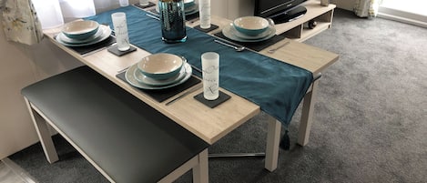 A dining area with a table set for four, a television, and a window with curtains.